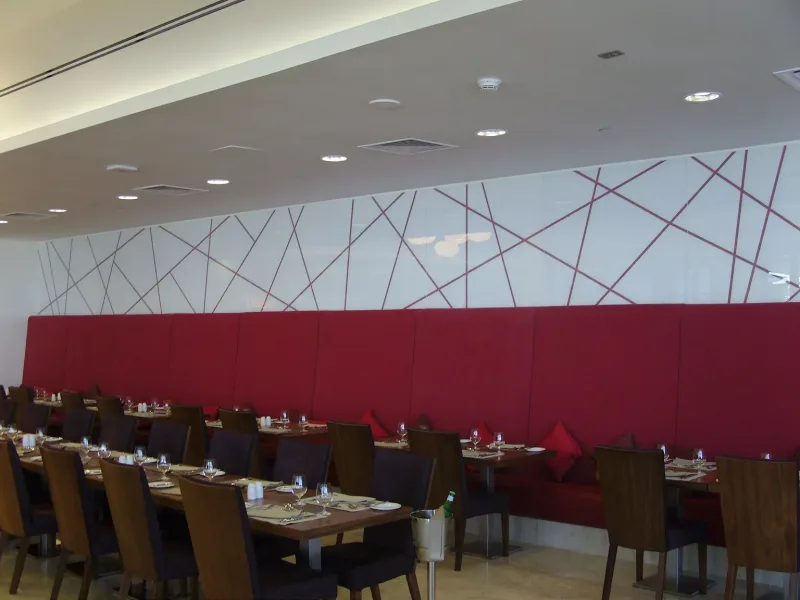 White back-painted glass wall with a red linear pattern above restaurant banquette seating