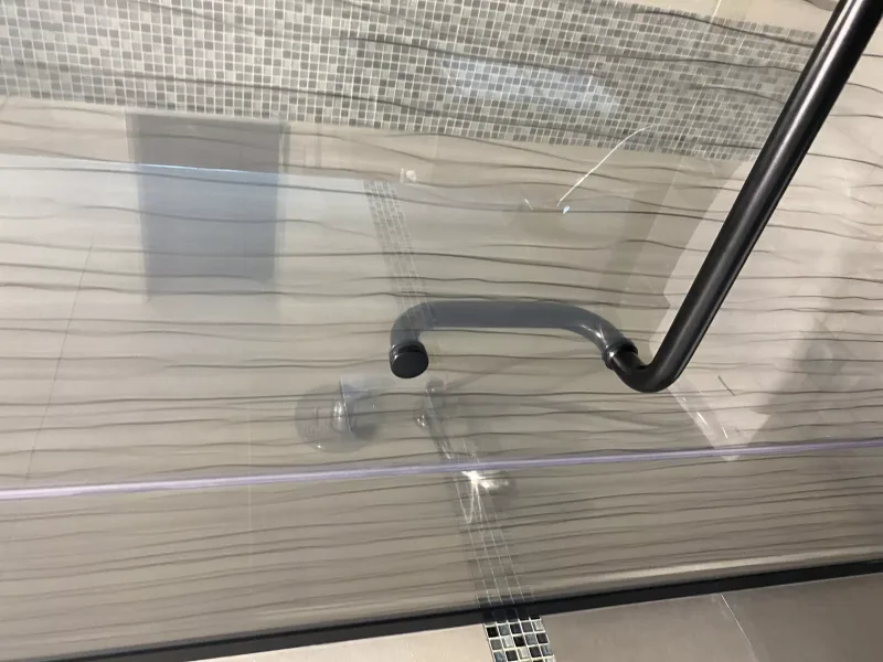 Close-up of matte black pull handle on wave-line patterned shower glass