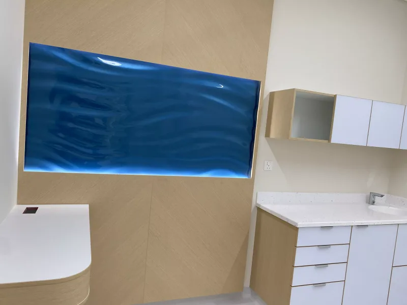 Backlit blue wavy textured glass panel set into an oak veneer wall in a healthcare interior
