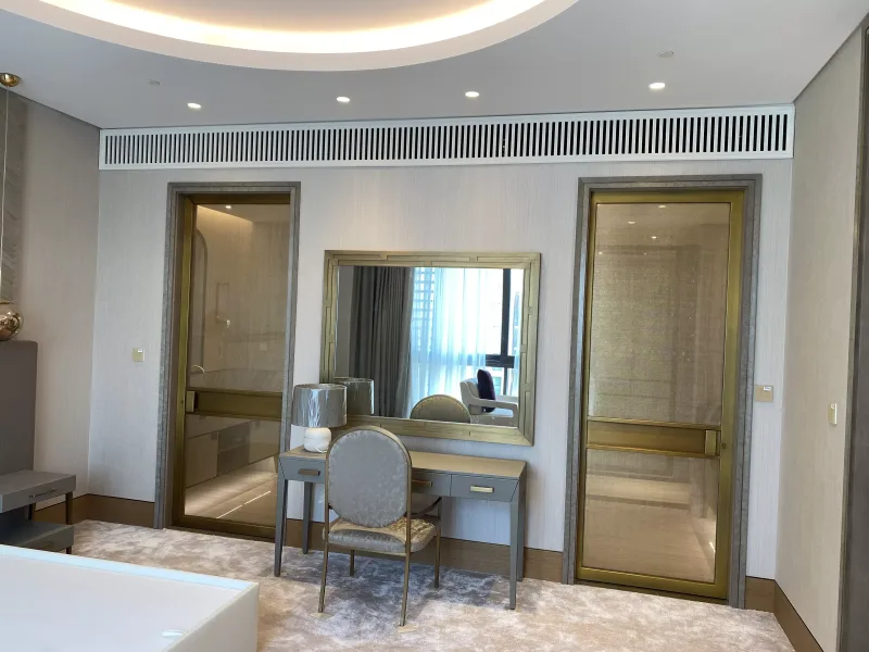 Brass-framed glass doors in a luxury suite bedroom with a matching brass-framed mirror