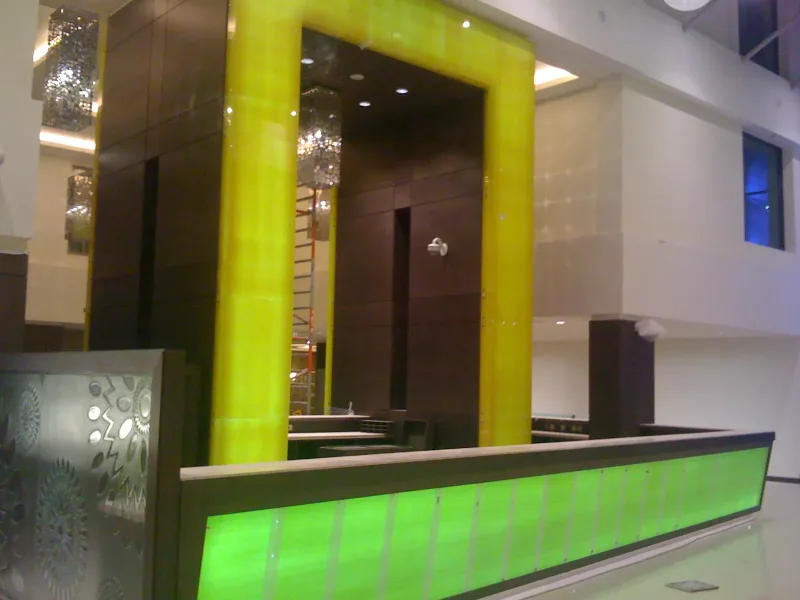 Green backlit glass reception counter and yellow glass portal in a hotel lobby with timber panelling
