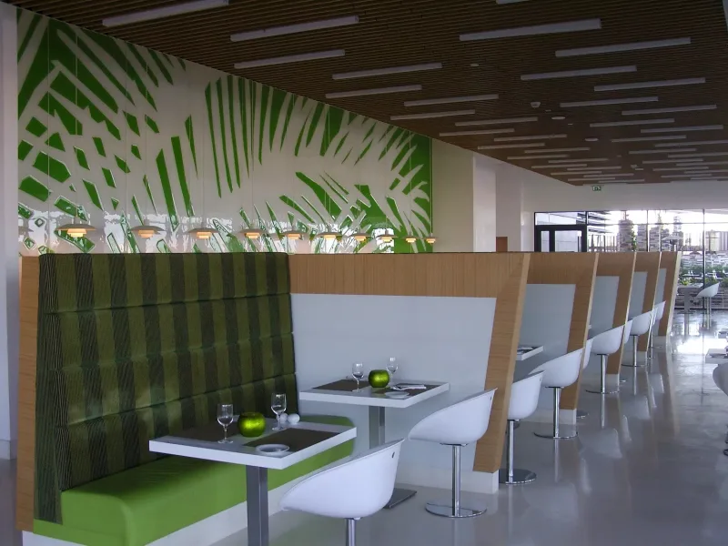 Green palm leaf pattern glass feature wall above restaurant booth seating