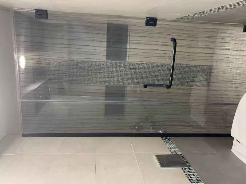 Wave-line patterned glass shower screen with black handle and hinges over a mosaic tile band