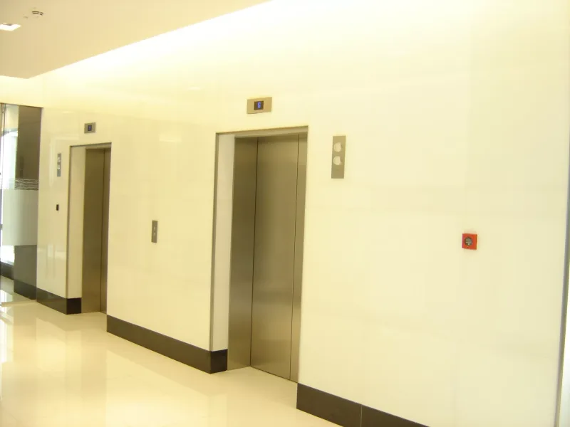 White back-painted glass wall cladding in a lift lobby with stainless steel lift doors