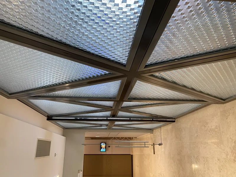 Woven-texture glass ceiling panels in a dark steel frame grid above a corridor
